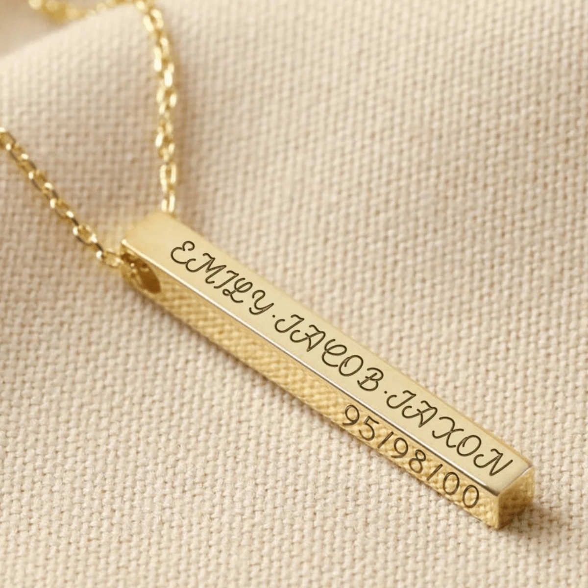 Gold bar necklace with engraved names and numbers on a beige fabric background