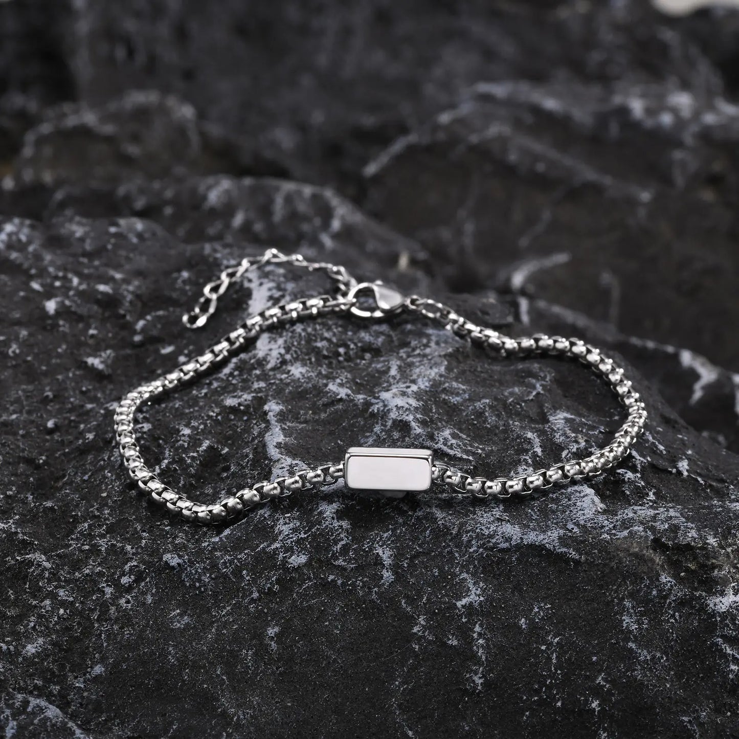 Silver bracelet with a rectangular charm on a dark stone surface