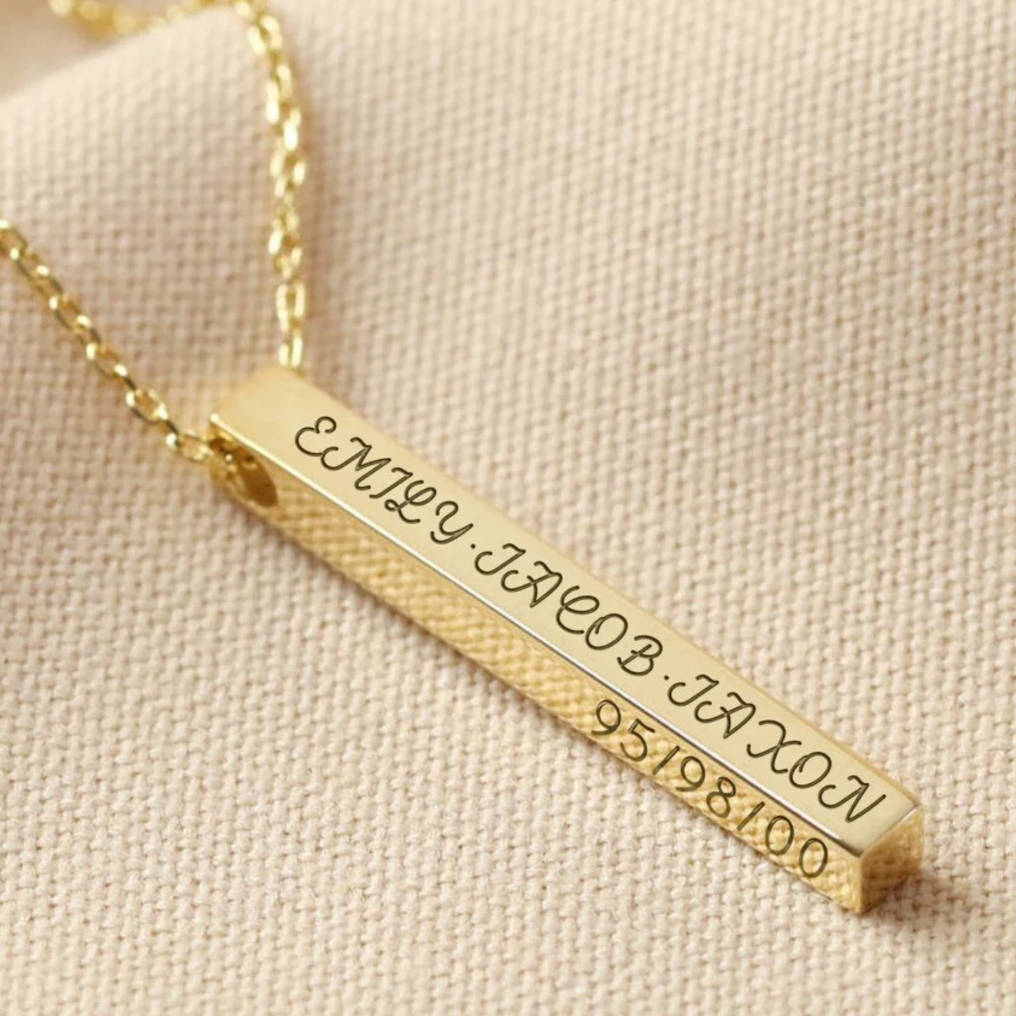 Gold bar necklace with engraved names and numbers on a beige fabric background