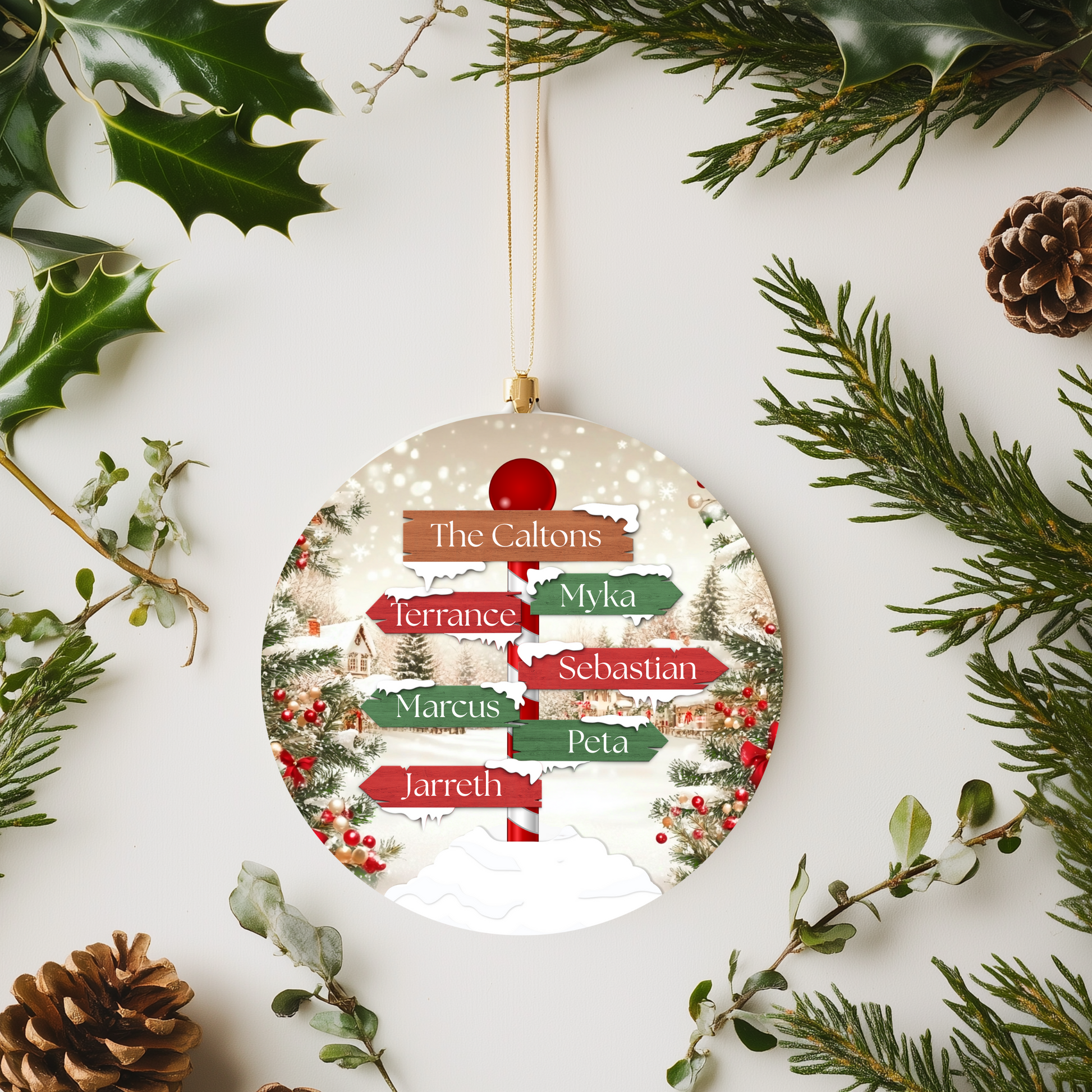 Round Christmas ornament with family names surrounded by greenery and pine cones on a white background