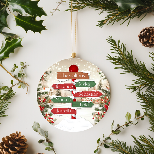 Round Christmas ornament with family names surrounded by greenery and pine cones on a white background