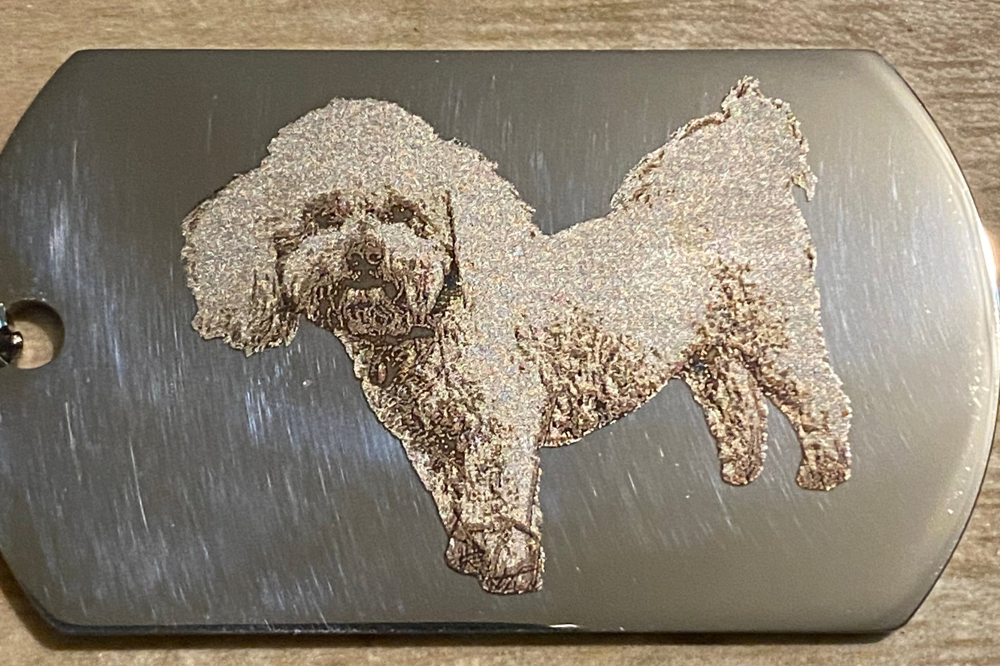 Metal dog tag with engraved bear design on a wooden surface