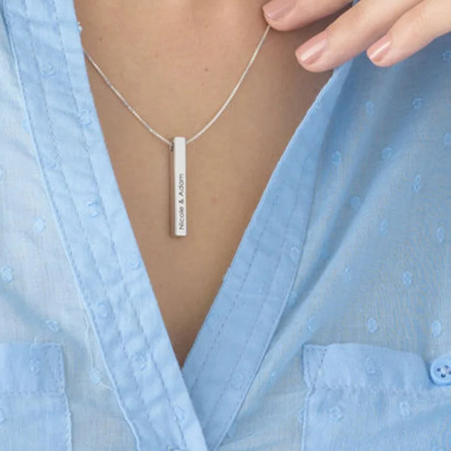 Person wearing a silver necklace with a bar pendant against a light blue fabric background