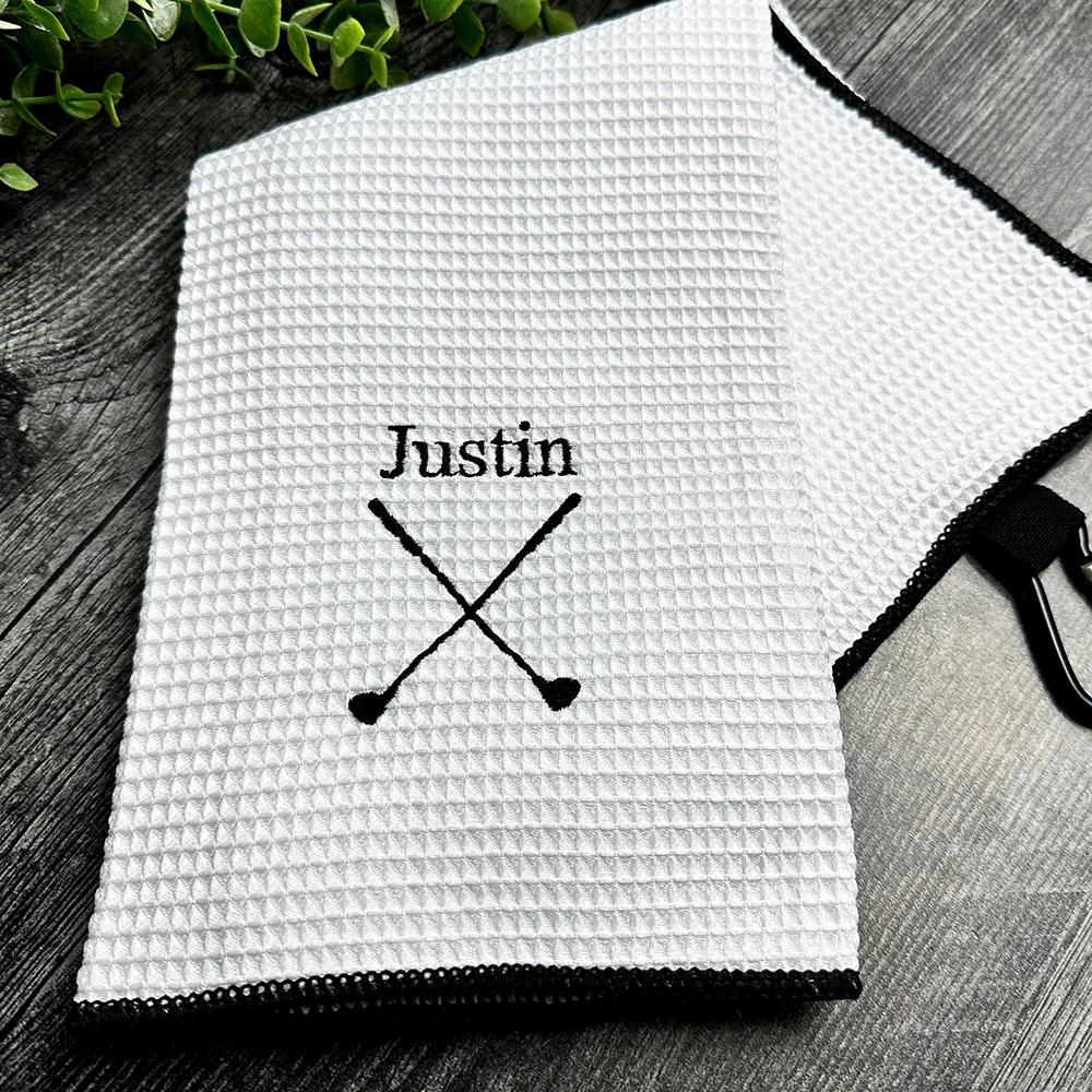White textured towel with 'Justin' and crossed paddles printed on it, placed on a wooden surface.