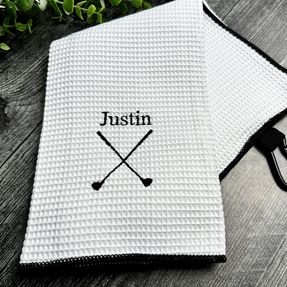 White textured towel with 'Justin' and crossed paddles printed on it, placed on a wooden surface.