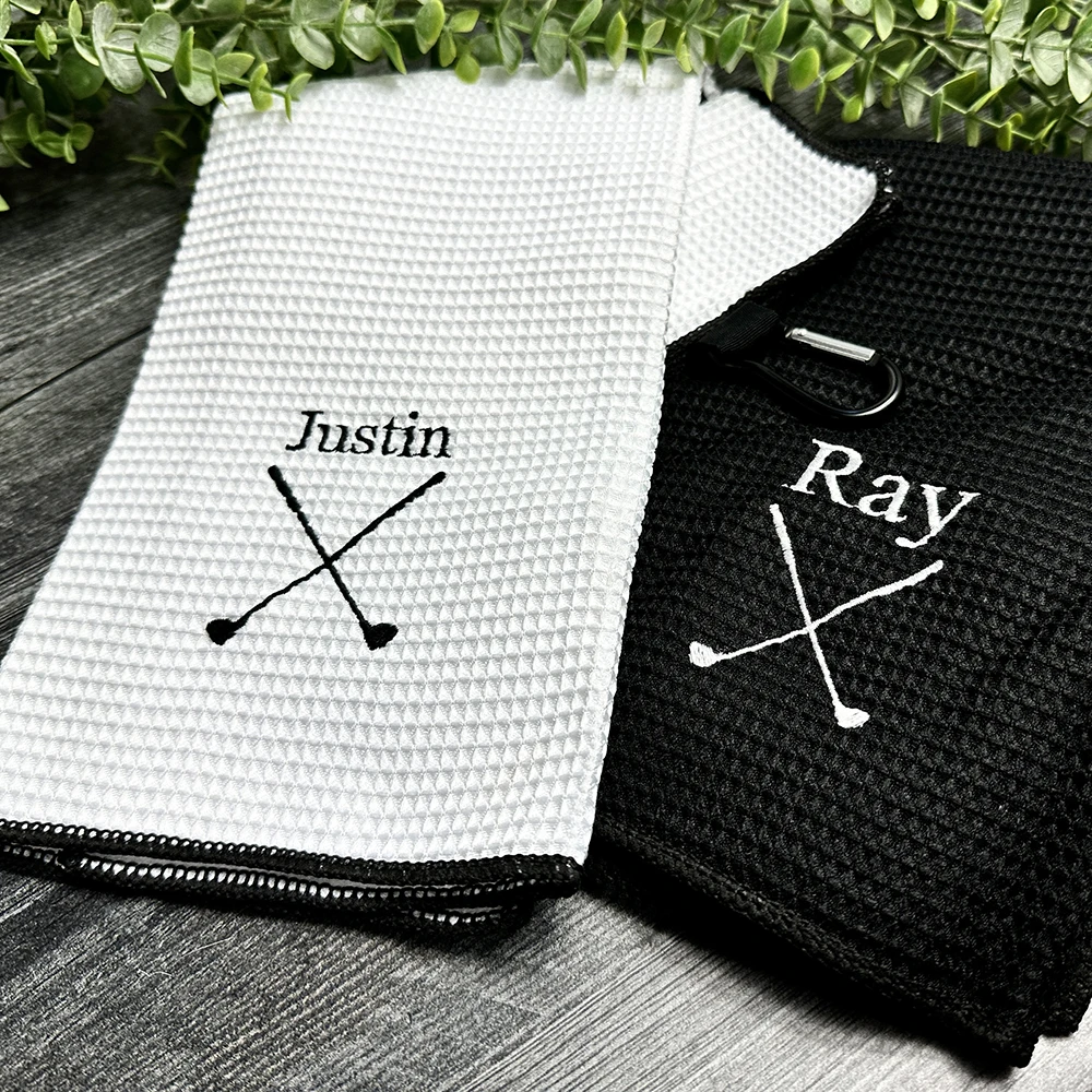 Two waffle-textured towels, one white and one black, with personalized embroidery on a wooden surface.
