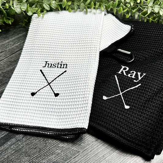 Two waffle-textured towels, one white and one black, with personalized embroidery on a wooden surface.