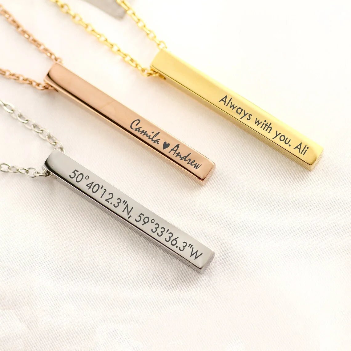 Three bar-shaped necklaces with engraved text on a light background