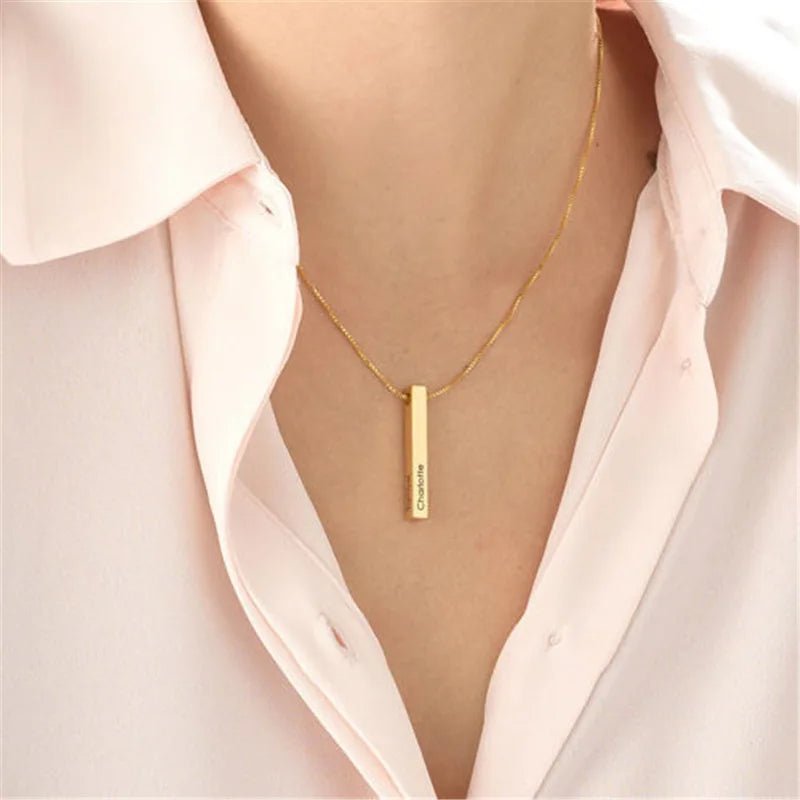 Gold necklace with a vertical pendant worn by a person in a light pink shirt.