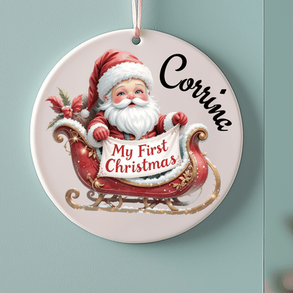 Decorative Christmas ornament with Santa Claus and 'My First Christmas' text on a light blue background.
