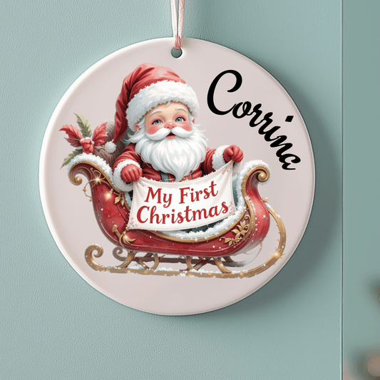 Decorative Christmas ornament with Santa Claus and 'My First Christmas' text on a light blue background.