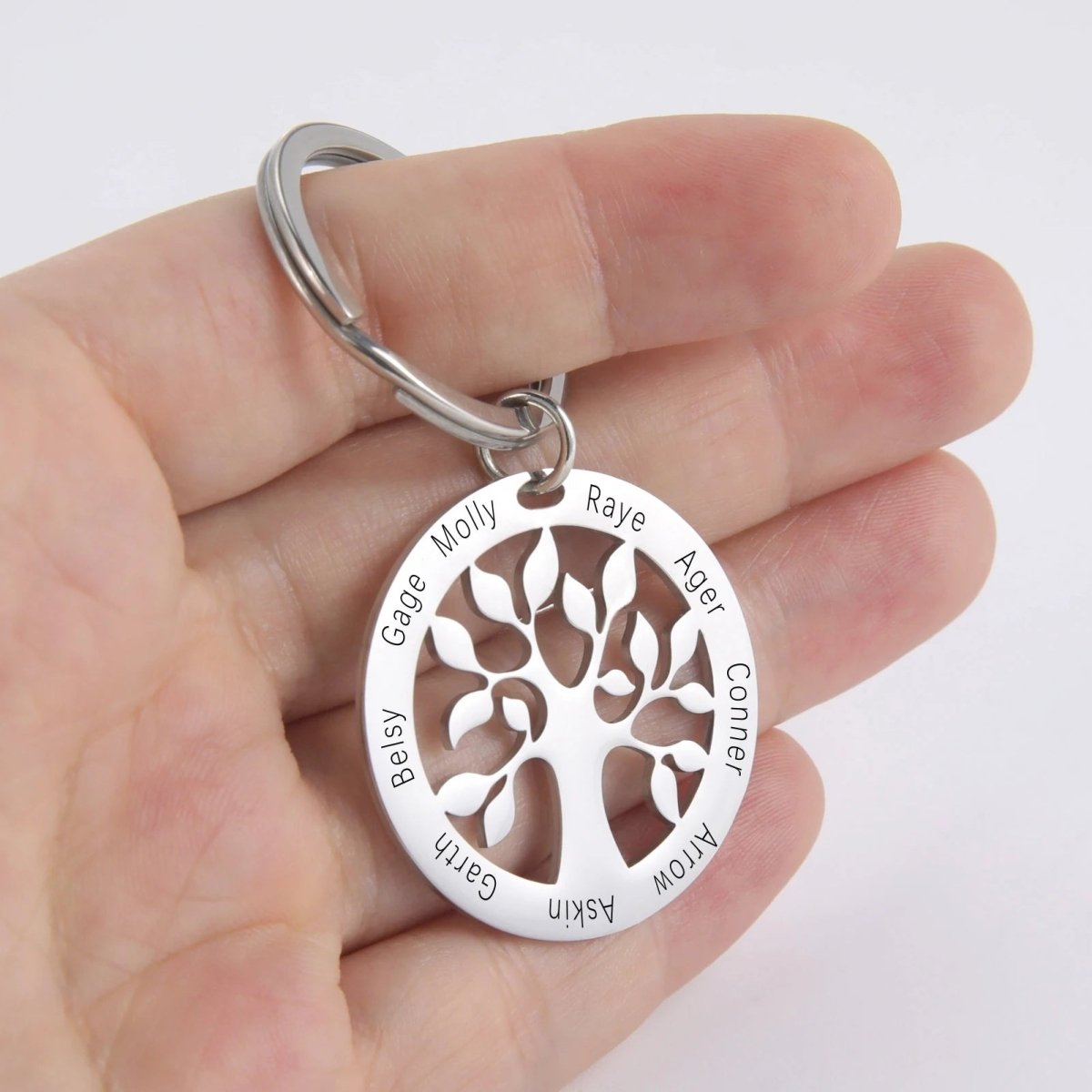 Silver keychain with tree design and engraved names held in a hand against a white background
