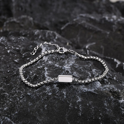 Silver bracelet with a rectangular charm on a dark stone surface